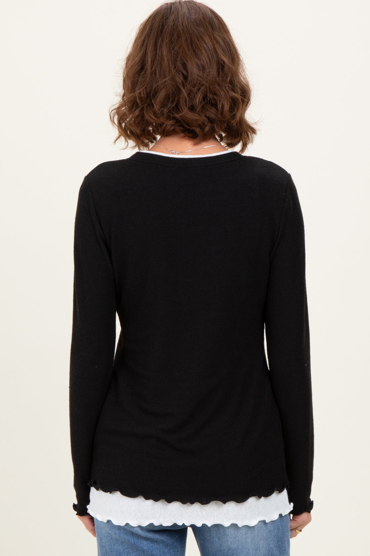 woman wearing a black long sleeve top with a scalloped hem layered over a white shirt, viewed from the back