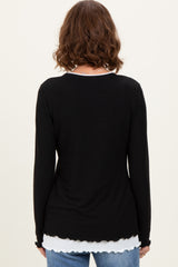 woman wearing a black long sleeve top with a scalloped hem layered over a white shirt, viewed from the back