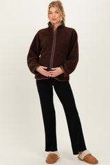 woman wearing a brown fleece maternity jacket and black maternity pants, holding her baby bump