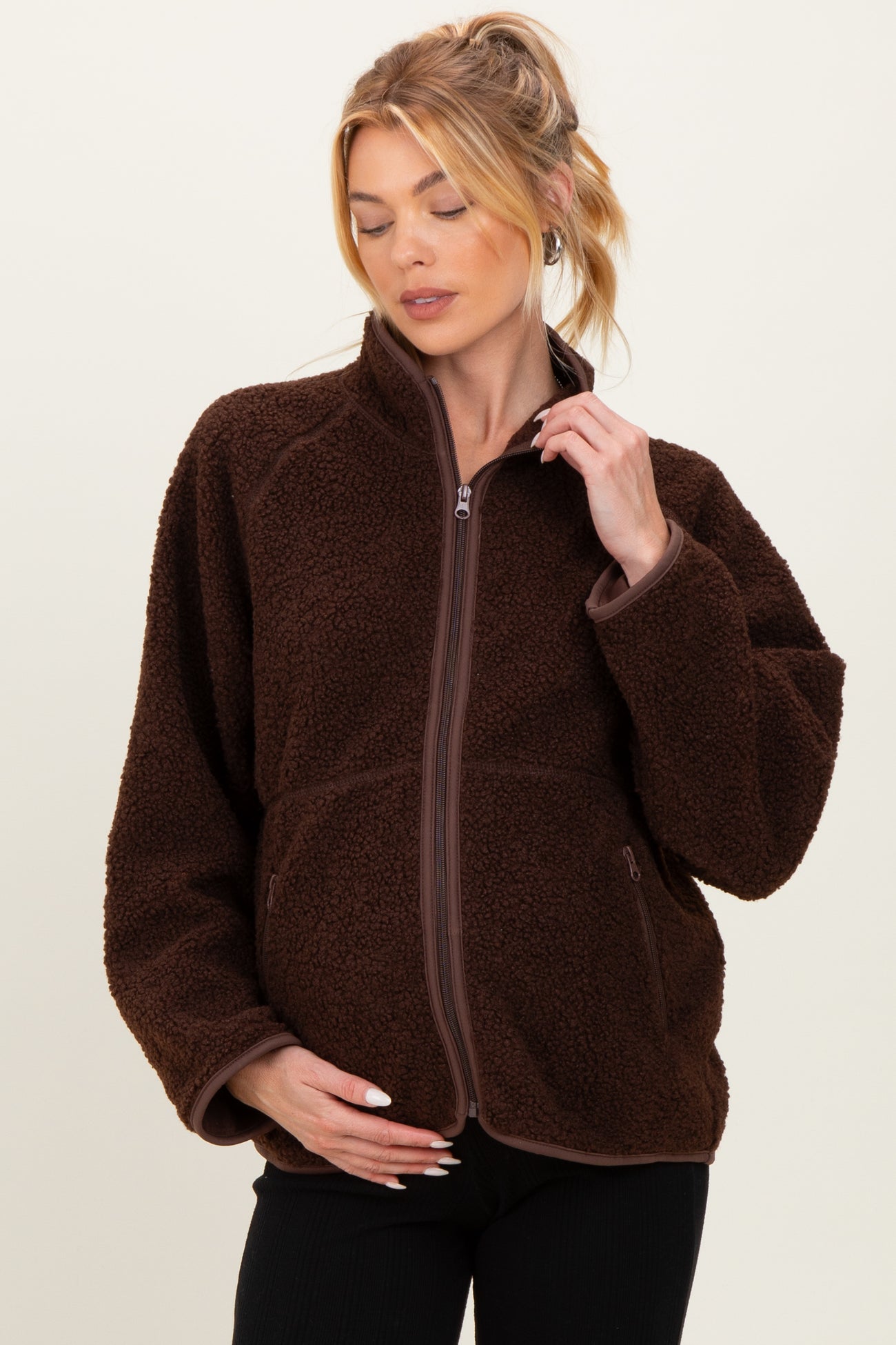 woman wearing a brown maternity fleece jacket with a quarter zip, holding her baby bump