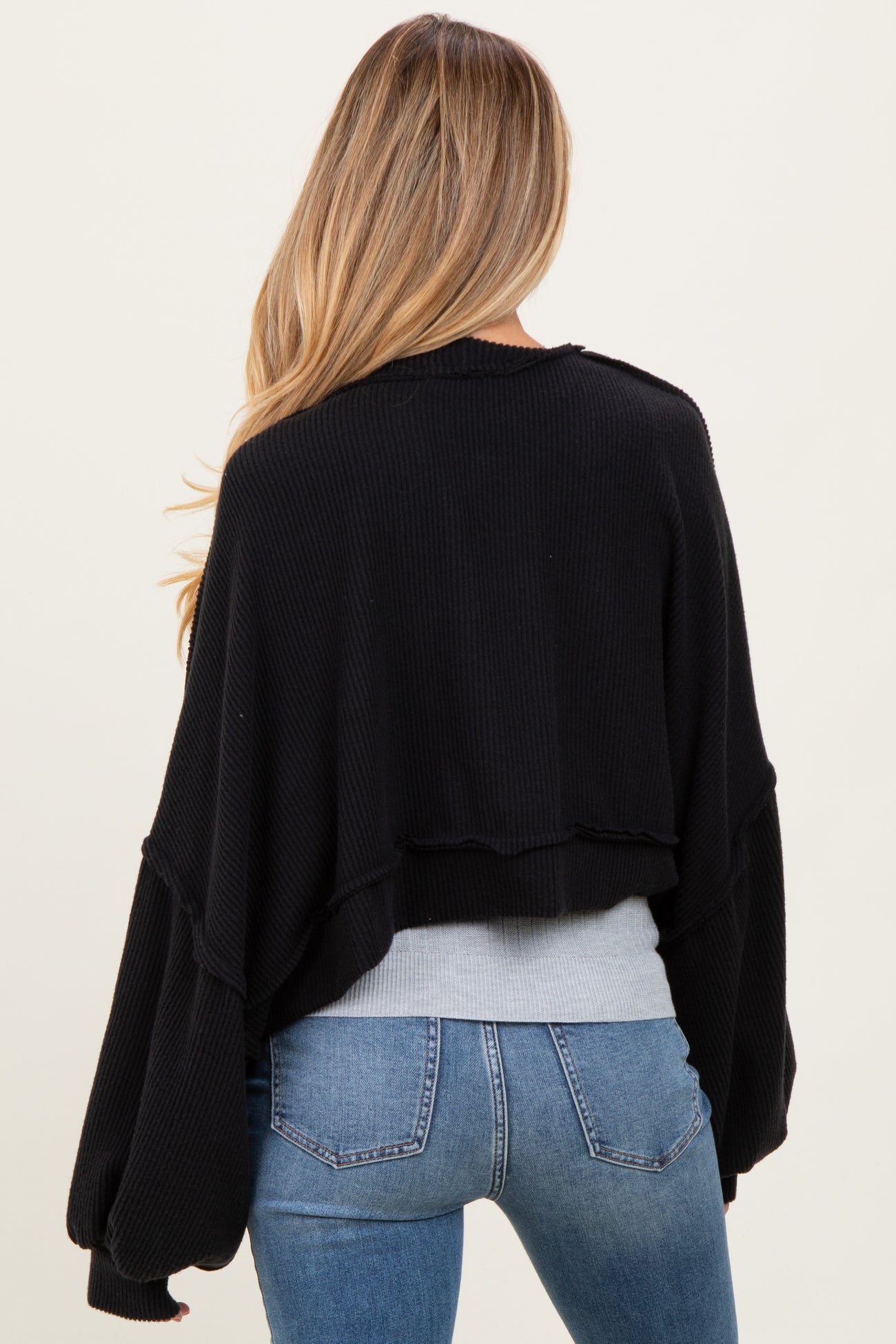 woman wearing a black cropped maternity sweater with wide sleeves, seen from the back, paired with blue jeans
