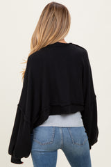 woman wearing a black cropped maternity sweater with wide sleeves, seen from the back, paired with blue jeans