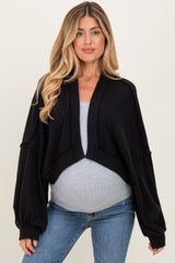woman wearing a black cropped maternity cardigan over a light gray top and showing her baby bump with jeans