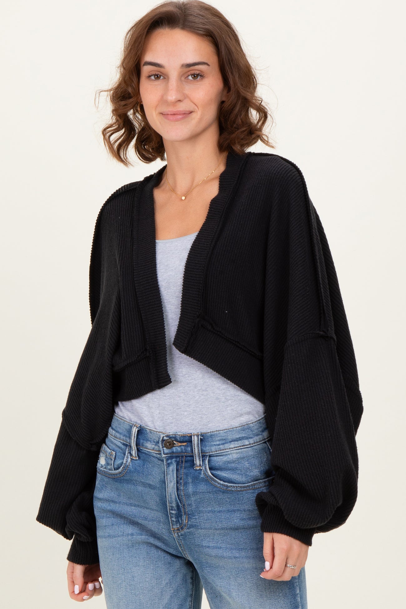 woman wearing a black cropped cardigan with balloon sleeves over a gray top and blue jeans