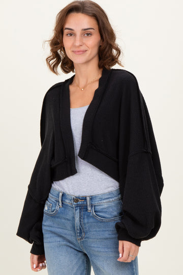 woman wearing a black cropped cardigan with balloon sleeves over a gray top and blue jeans