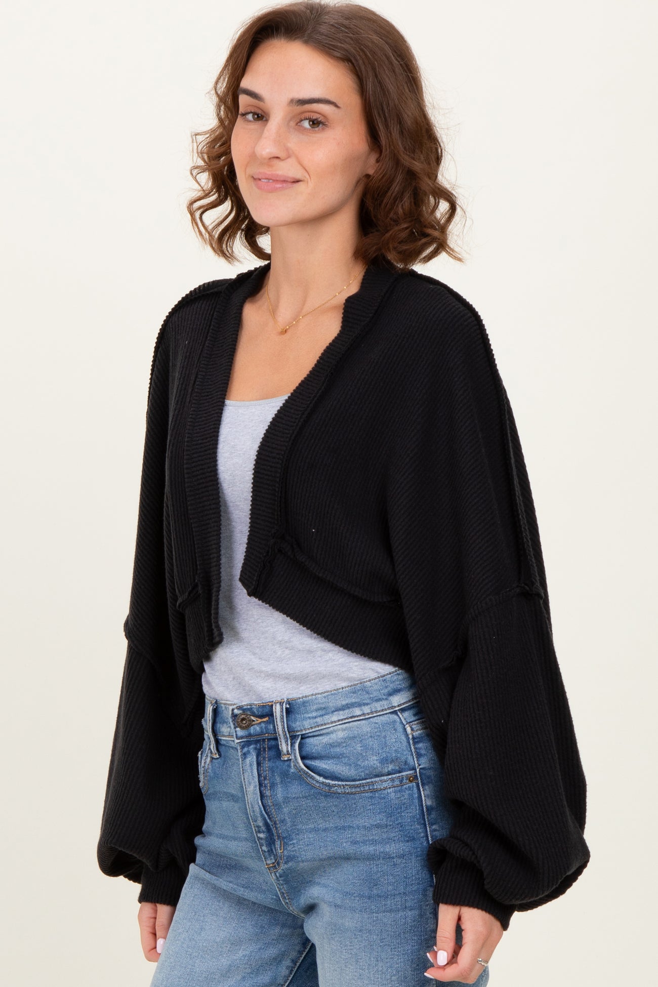 woman wearing a black cropped cardigan with oversized sleeves and a gray tank top, paired with blue jeans
