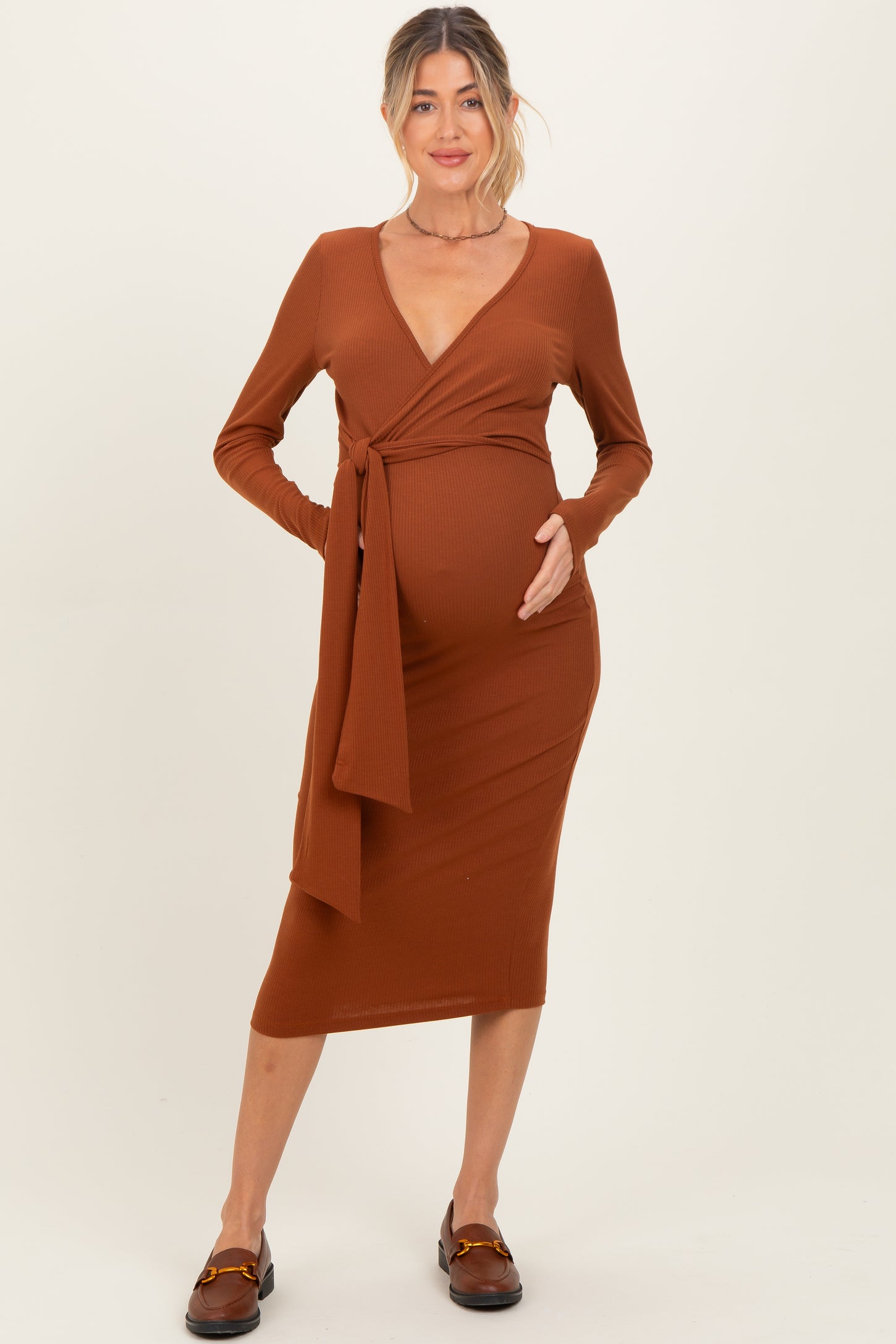 woman wearing a rust brown long sleeve maternity wrap dress and holding her baby bump