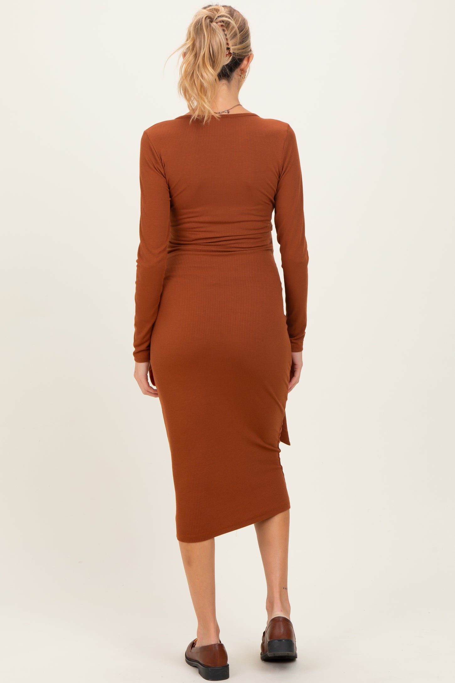 woman wearing a rust long sleeve maternity dress with a fitted silhouette and side slit, showing a baby bump