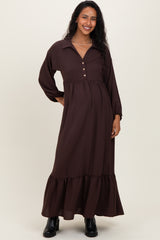 woman wearing a dark brown maternity maxi dress with a collar, button details, and a ruffled hem, showcasing her baby bump