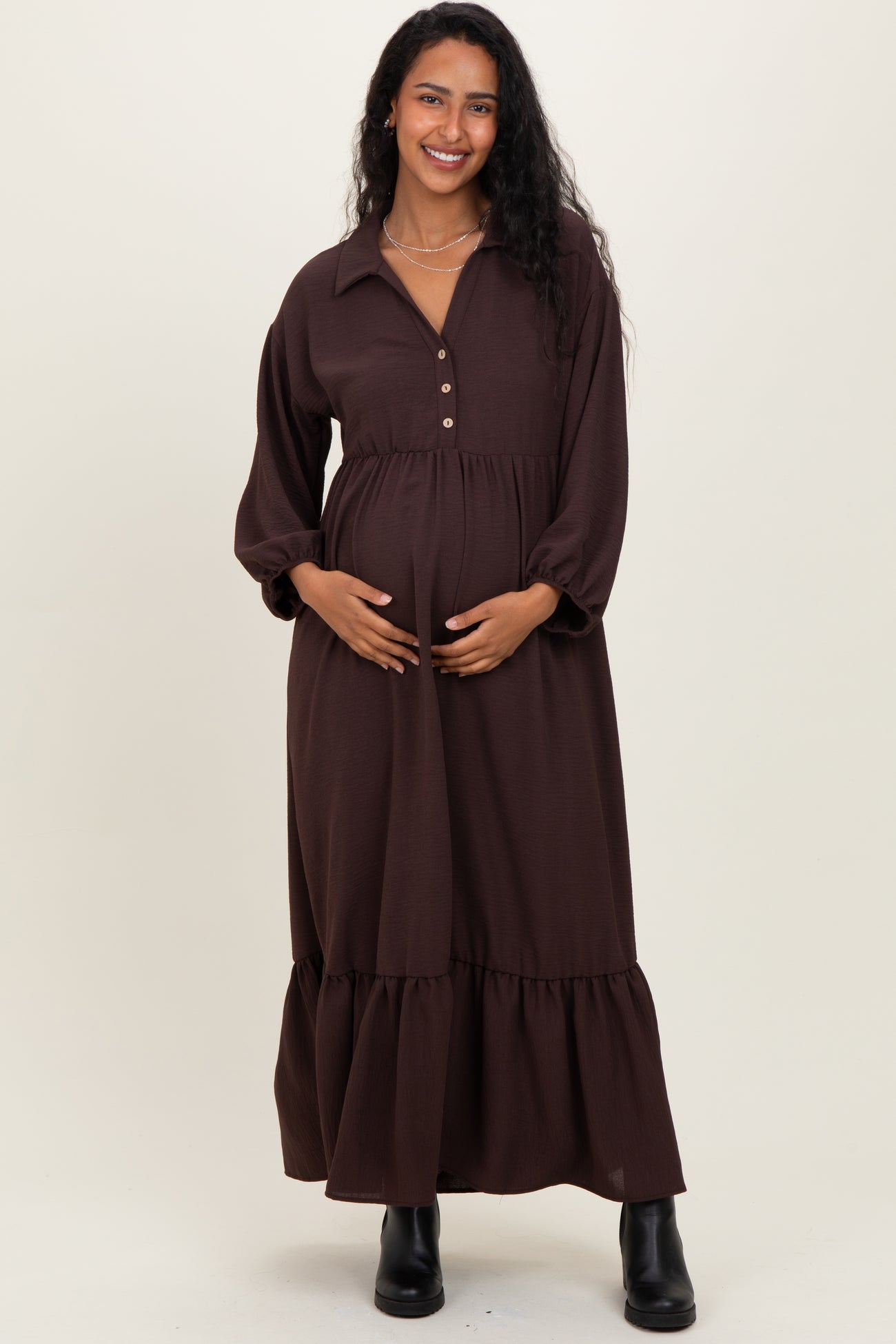 woman wearing a brown maternity dress with a button-up collar and tiered skirt, gently cradling her baby bump