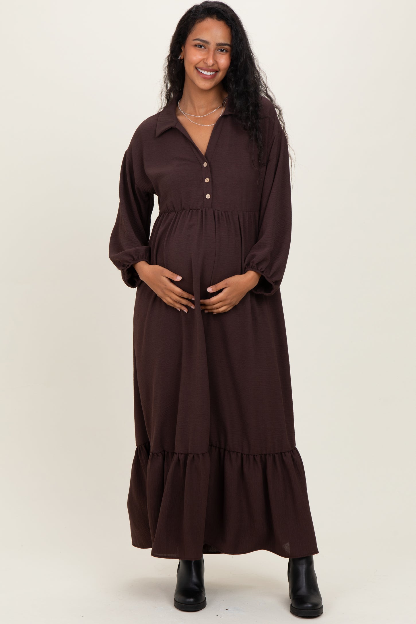 woman wearing a brown maternity dress with a button-up collar and tiered skirt, gently cradling her baby bump