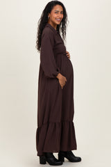 woman wearing a brown maternity maxi dress with long sleeves and a ruffle hem, holding her baby bump