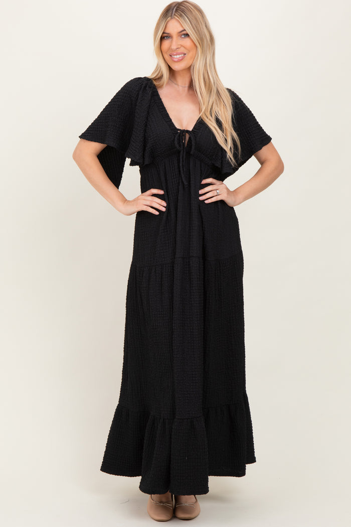 woman wearing a black maxi dress with short sleeves and a tie front detail, styled with a tiered skirt