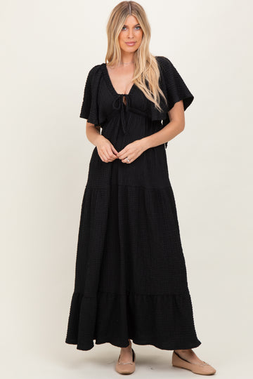 woman wearing a black tiered maxi dress with short sleeves and a tie front detail