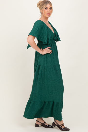 woman wearing a dark green tiered maxi dress with flutter sleeves and a tie front detail