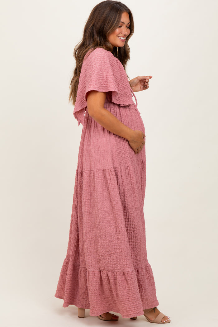 woman wearing a pink maternity maxi dress with flutter sleeves and pockets, showing her baby bump