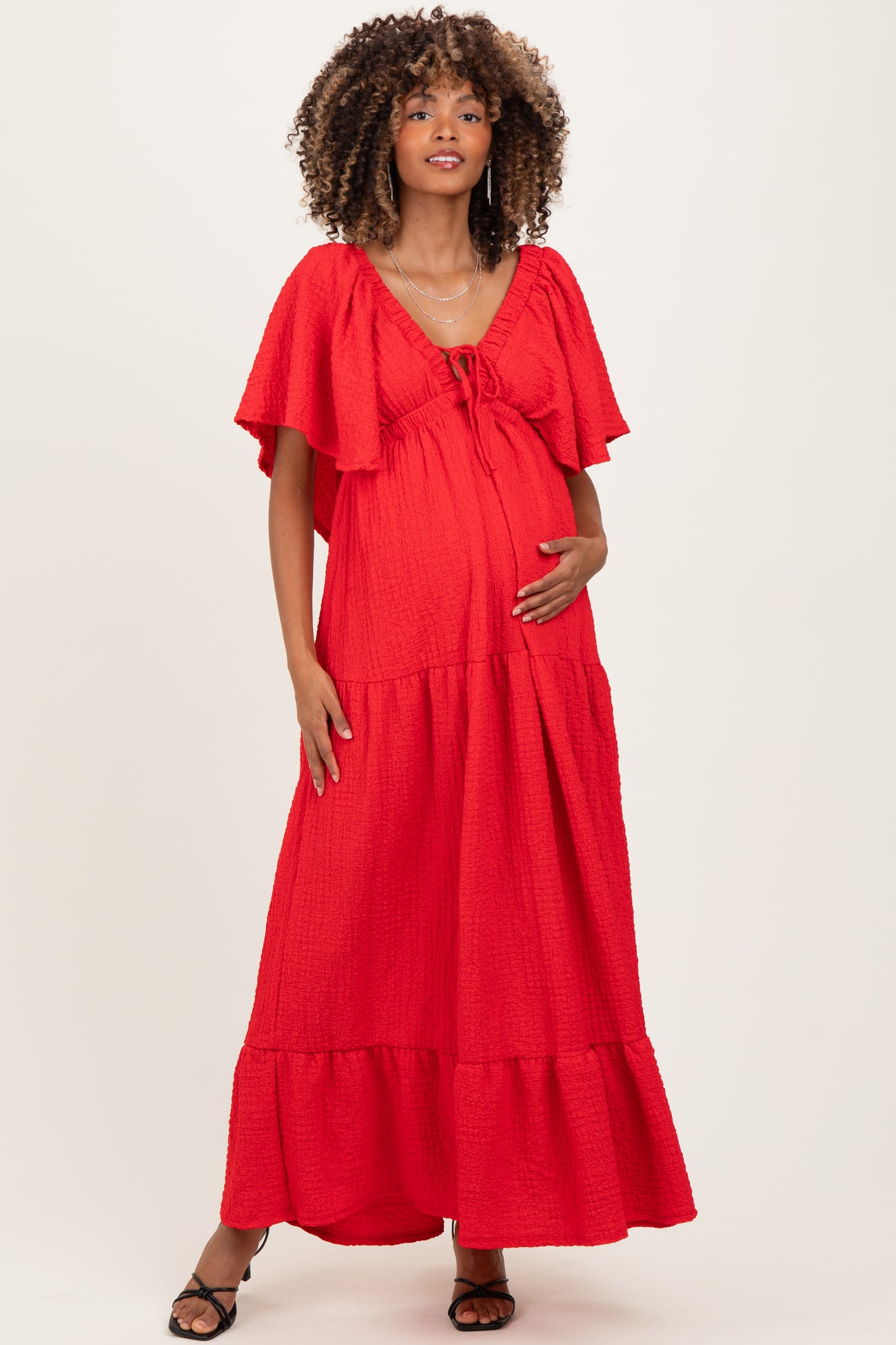 woman wearing a red maternity maxi dress with flutter sleeves and a drawstring neckline, holding her baby bump
