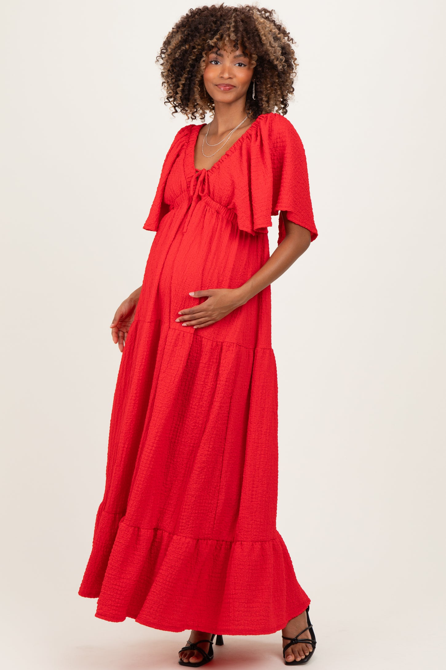 woman wearing a red maternity maxi dress with a tie front and short flutter sleeves, showing her baby bump