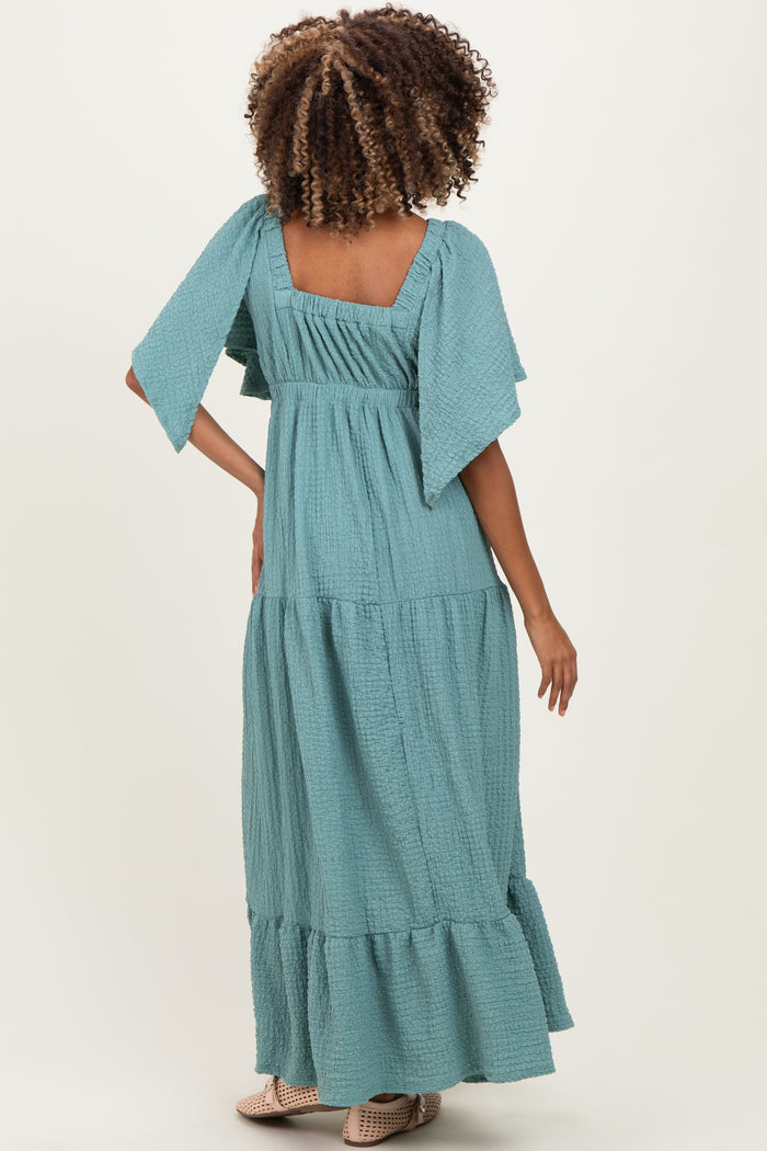 woman wearing a teal maternity maxi dress with flutter sleeves and tiered ruffle hem