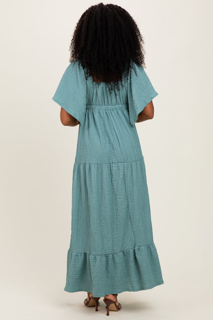 woman wearing a flowy teal maxi dress with short flutter sleeves and tiered ruffle hem