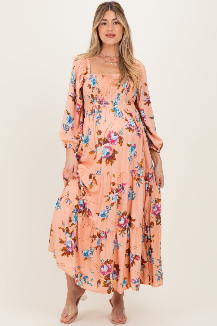 woman wearing a blush floral maternity maxi dress with puff sleeves and a smocked bodice, displaying her baby bump