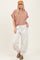 woman wearing a beige striped oversized top and cream jogger pants, styled with a brown cap and sandals