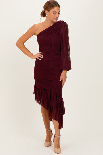 woman wearing a one-shoulder burgundy dress with ruched detailing and a ruffled hem