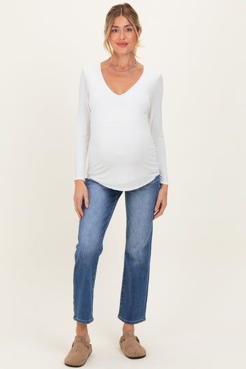 woman wearing a white long sleeve maternity top and blue jeans, showing her baby bump