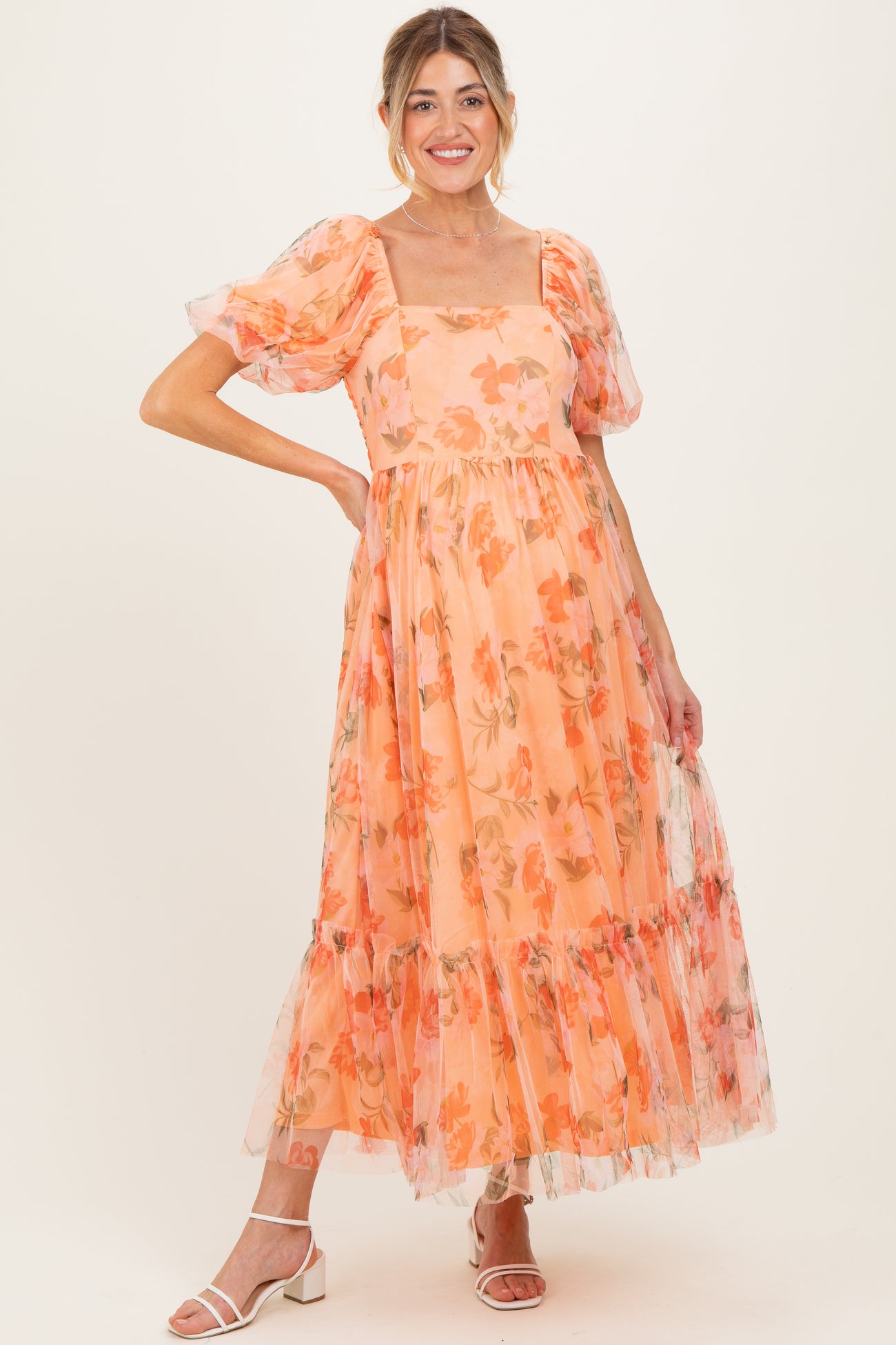 woman wearing a floral maternity dress in peach with puff sleeves and a tiered skirt, showcasing her baby bump