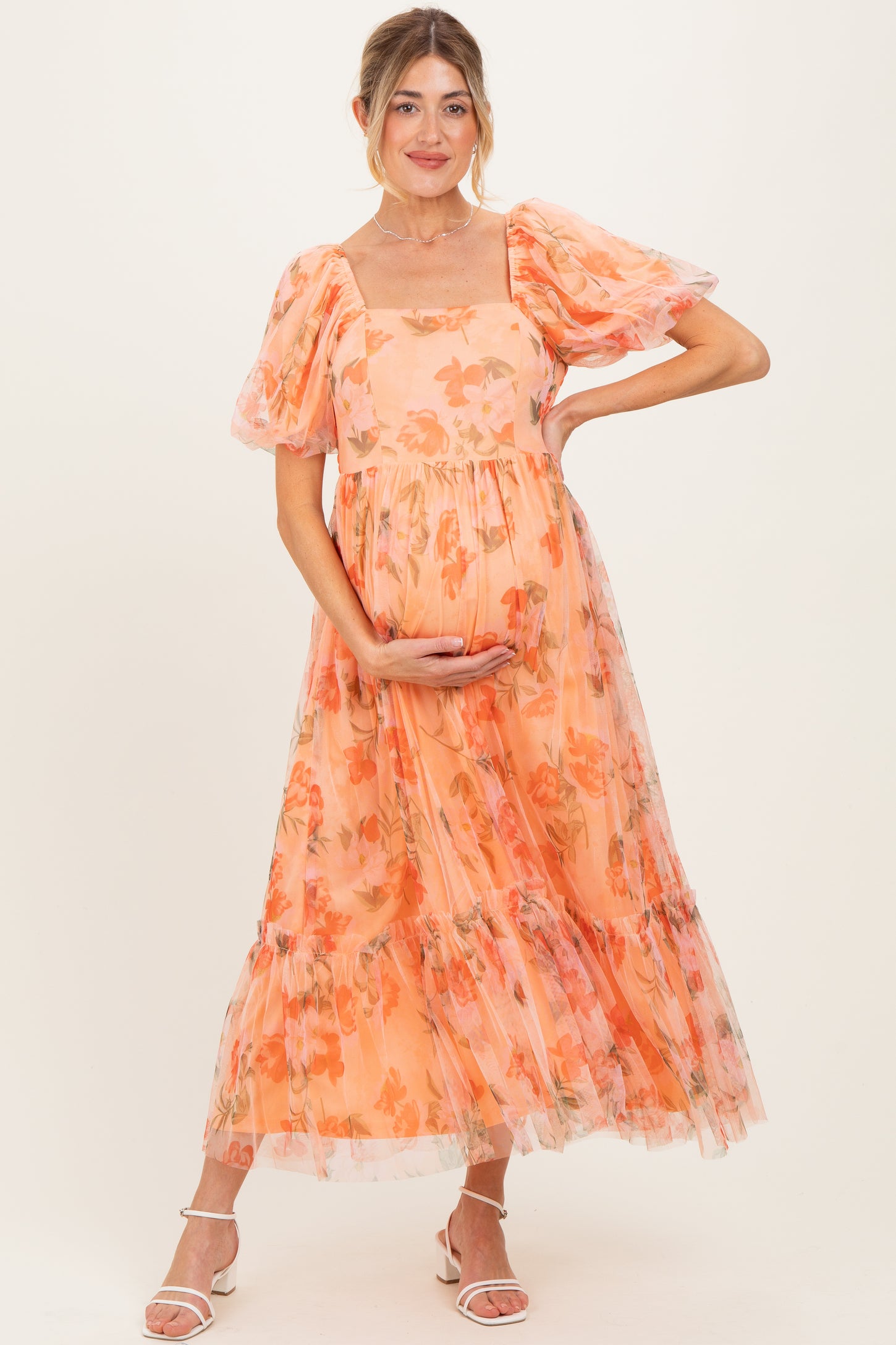 woman wearing a coral floral maternity dress with puffy sleeves and holding her baby bump