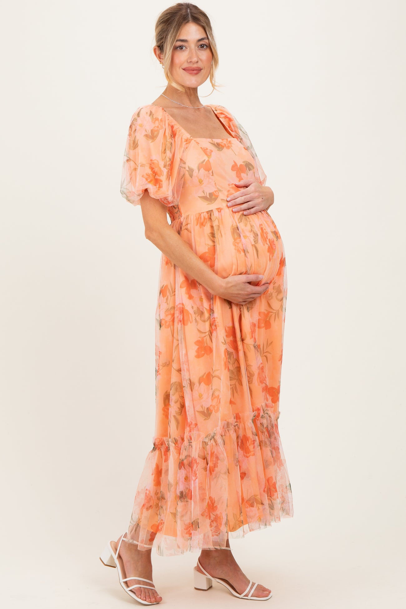 woman wearing an orange floral maternity dress with puff sleeves and a tiered skirt, cradling her baby bump