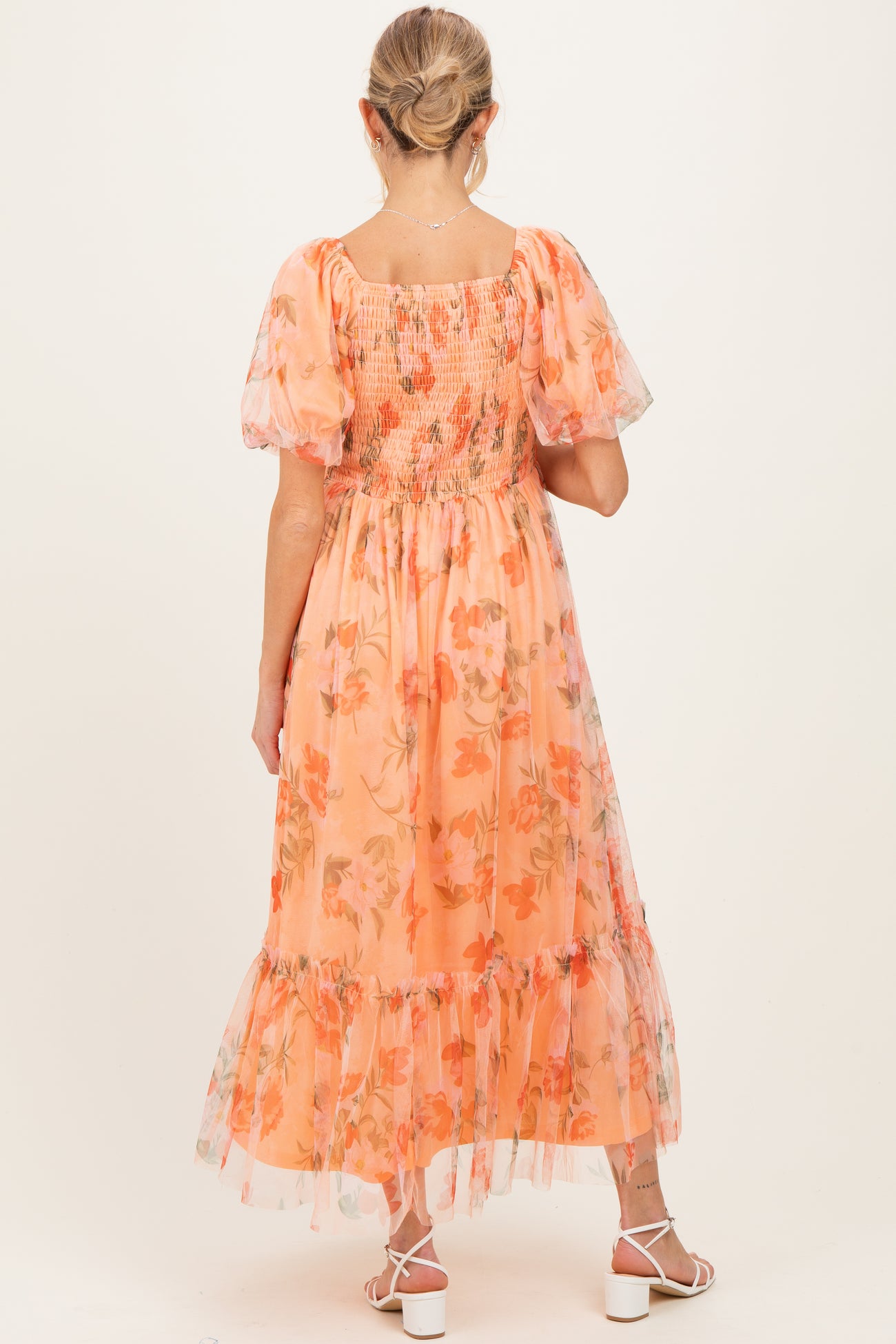 woman wearing a peach floral maternity dress with puff sleeves and a smocked bodice, showing back view