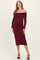 woman wearing a burgundy off-the-shoulder maternity dress with long sleeves and a bow detail, showing her baby bump