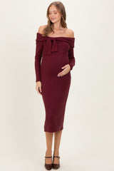 woman wearing a burgundy ribbed off-the-shoulder maternity dress with a bow detail and a visible baby bump