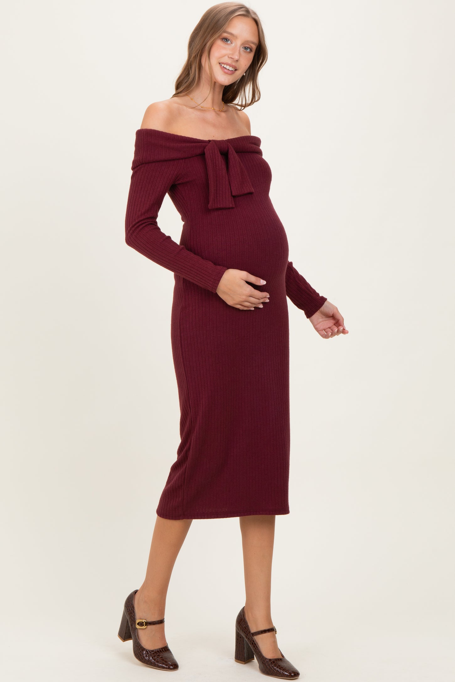 woman wearing a burgundy off-the-shoulder maternity dress with a bow detail and a visible baby bump
