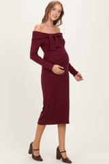 woman wearing a burgundy off-the-shoulder maternity dress with a bow detail and a visible baby bump