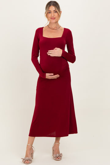 woman wearing a burgundy long sleeve maternity dress with a square neckline and holding her baby bump