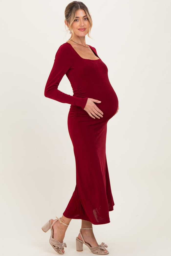 woman wearing a burgundy long sleeve maternity dress, cradling her baby bump with a soft smile