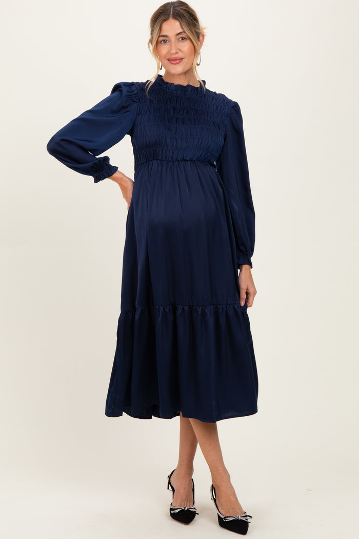 woman wearing a navy blue maternity dress with a smocked bodice and tiered hem, showcasing her baby bump