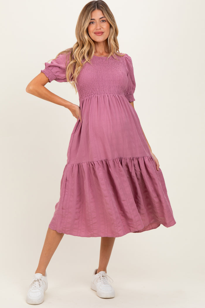 woman wearing a dusty rose maternity dress with short puff sleeves and a tiered skirt, showing her baby bump