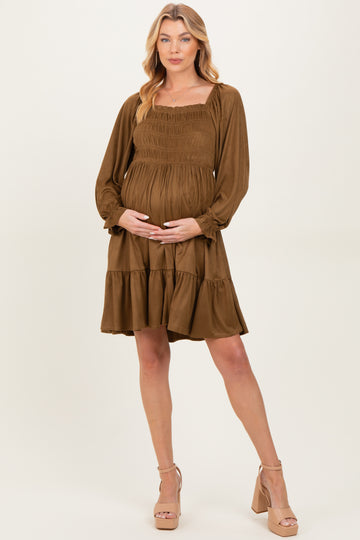 woman wearing a brown long sleeve maternity dress with a smocked bodice and ruffled hem, holding her baby bump