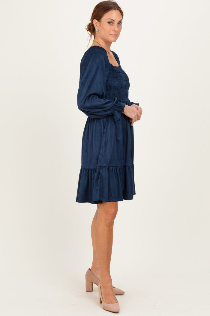 woman wearing a navy blue smocked dress with puff sleeves and a tiered ruffle hem, standing in profile with heels