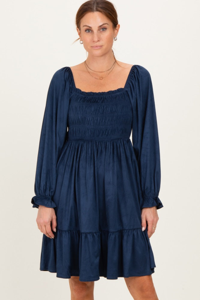 woman wearing a navy blue smocked mini dress with long sleeves and a tiered skirt