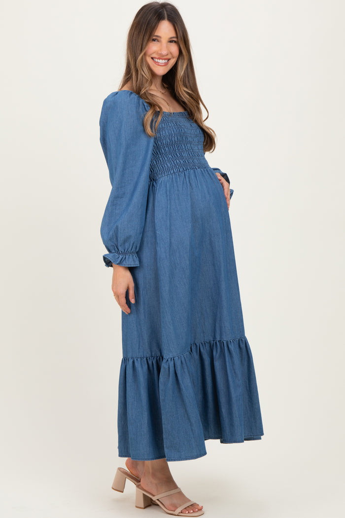 woman wearing a denim blue maternity dress with a smocked bodice and ruffled hem, holding her baby bump