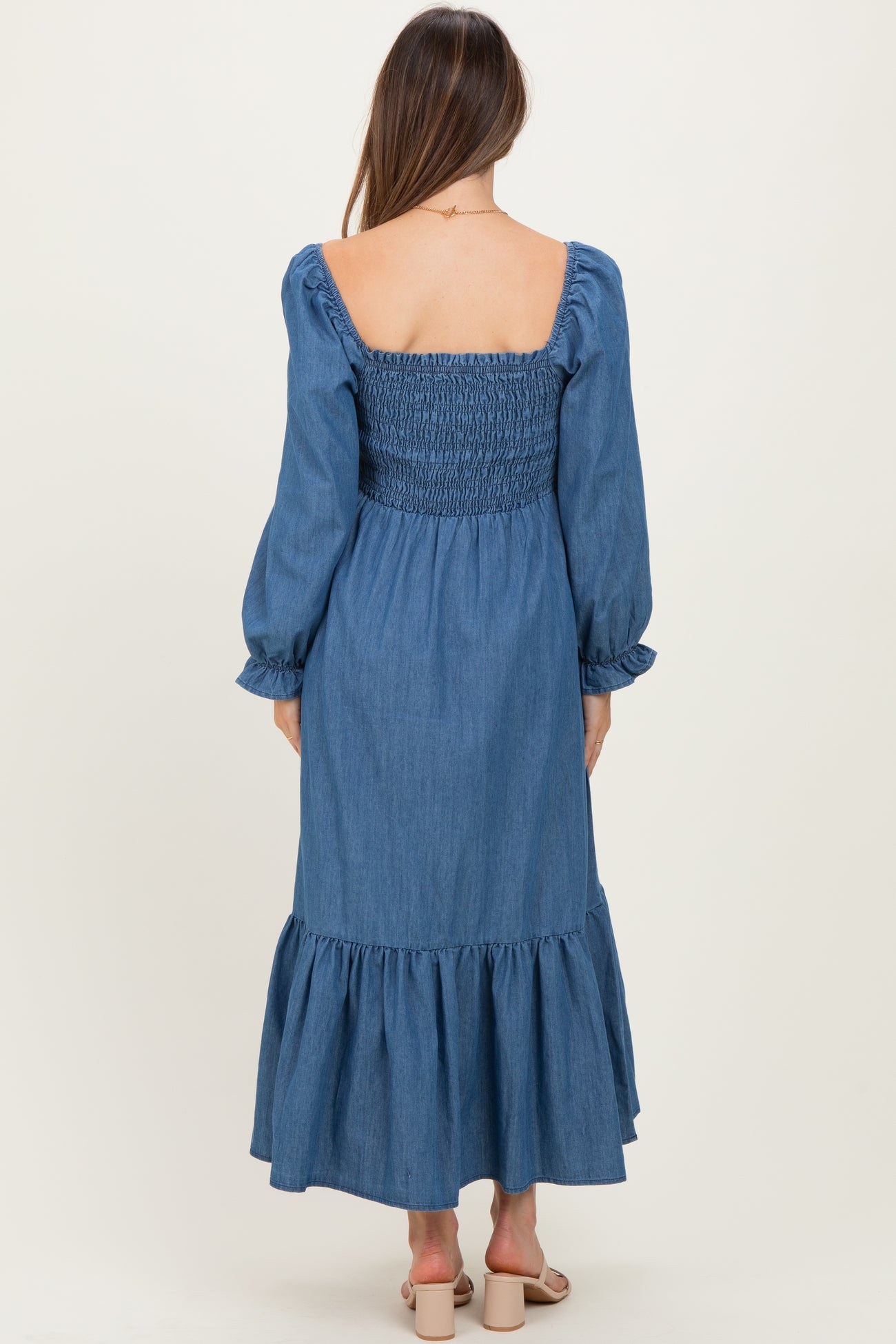 woman wearing a denim smocked maternity dress with long sleeves and a ruffled hem