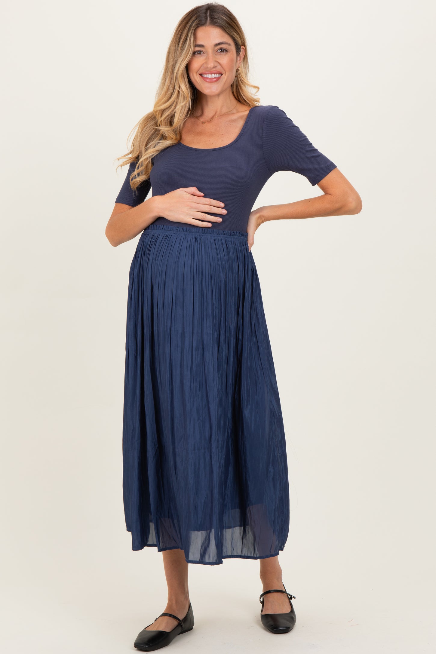 woman wearing a navy ribbed short sleeve maternity top and a pleated maxi skirt, holding her baby bump