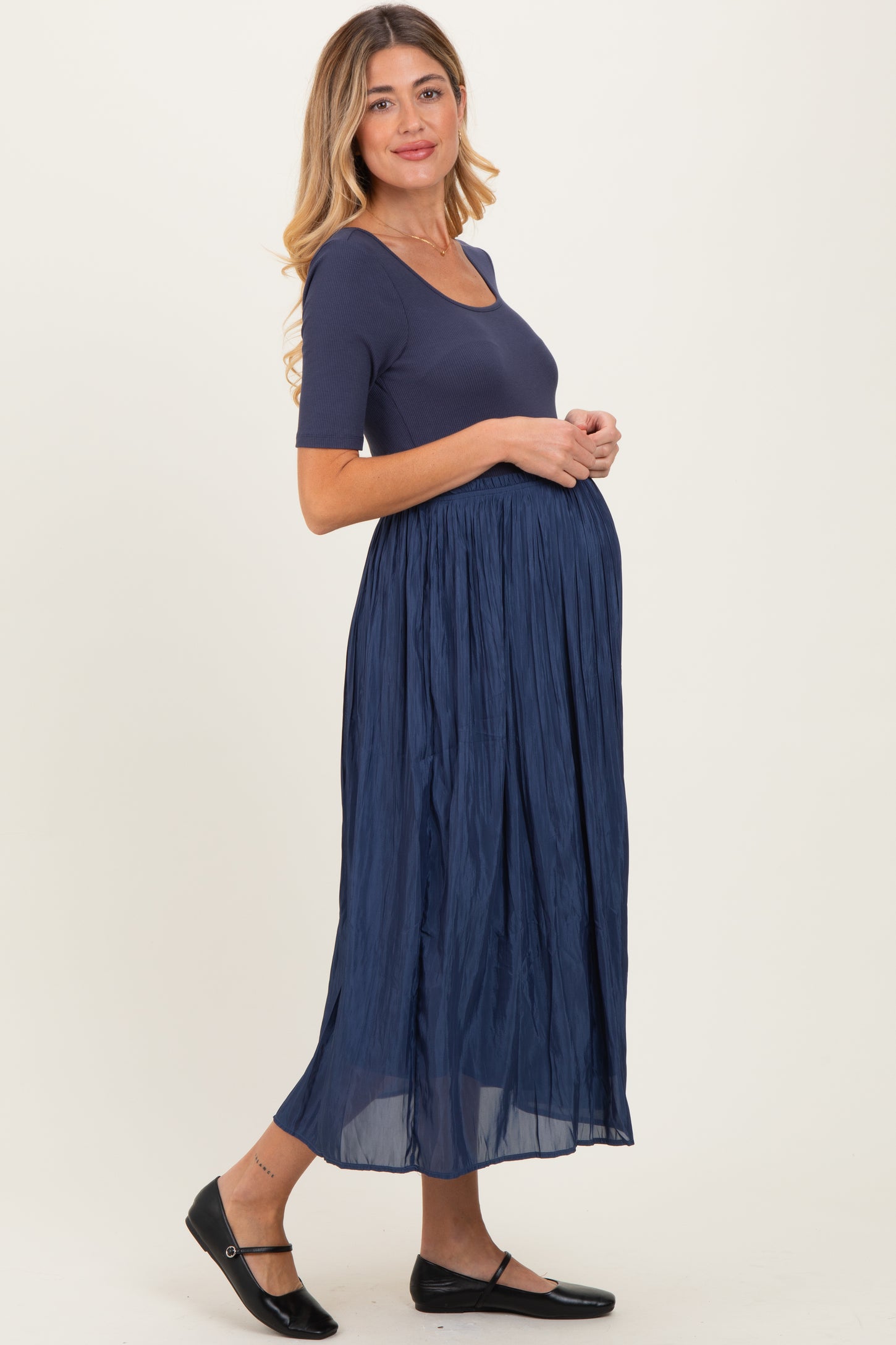 woman wearing a navy blue maternity dress with a fitted top and flowy skirt, showing her baby bump