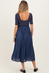 woman wearing a navy blue maternity dress with a fitted top and flowing skirt, showing a baby bump from the back
