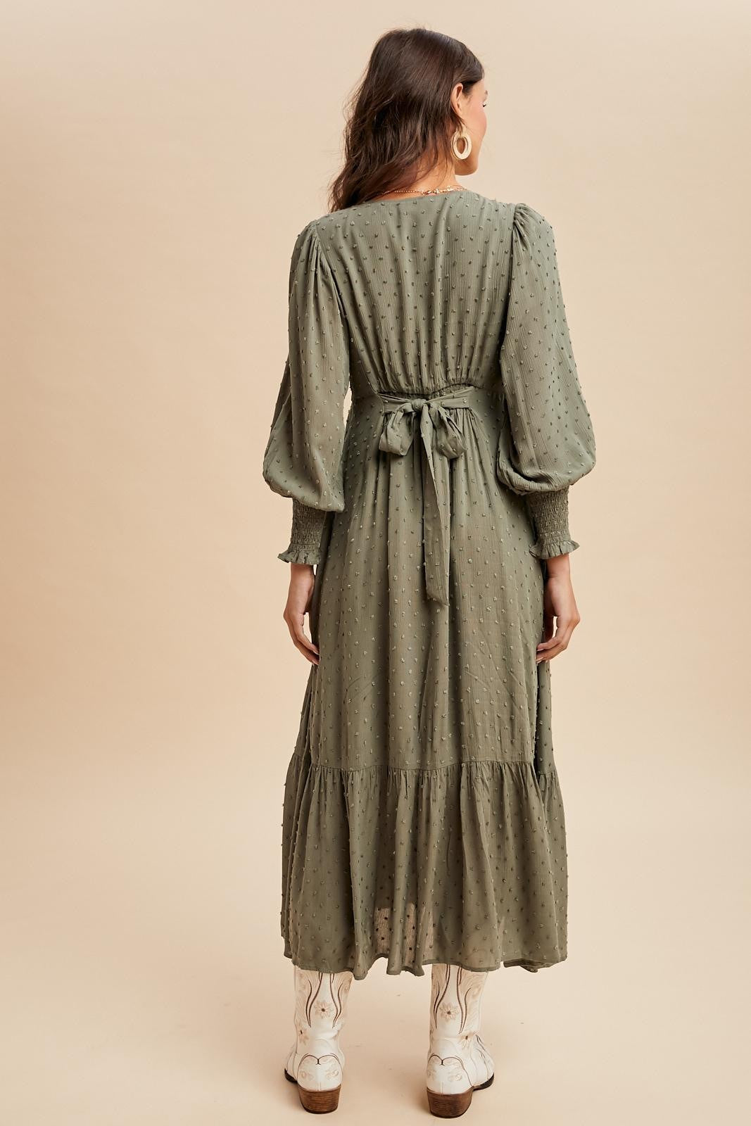 woman wearing a long olive green tiered maxi dress with puff sleeves and a tied waist detail, seen from the back
