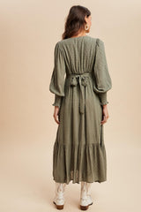 woman wearing a long olive green tiered maxi dress with puff sleeves and a tied waist detail, seen from the back